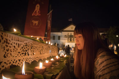 Woman looking at lit diyas at night