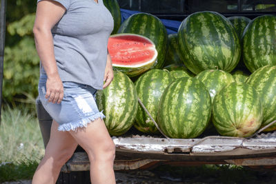 Midsection of woman walking by watermelons in trunk