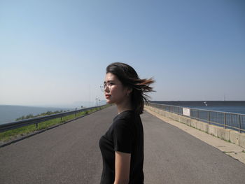 Side view of young woman standing on road against clear sky