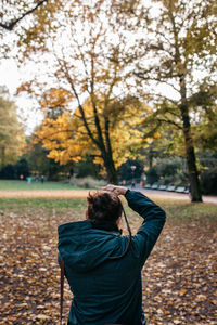 Rear view of female woman photographing trees at park during autumn