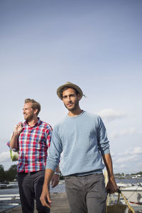Portrait of man carrying picnic basket while walking with friend on pier