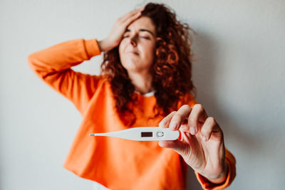 Sick mid adult woman showing thermometer while standing against wall