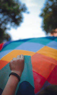 Cropped hand holding multi colored fabric against sky