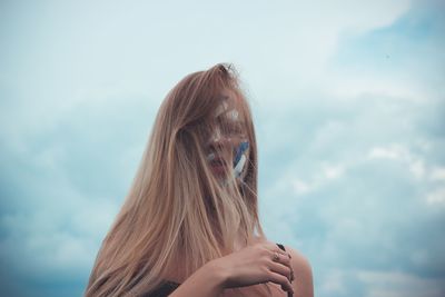 Young woman with blond messy hair standing against sky