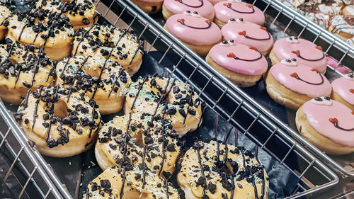 Chocolate and pink donuts with smiles in metal trays on a store shelf, close-up side view.