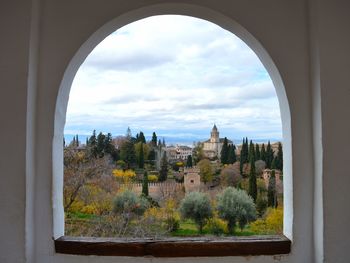 Trees and buildings against sky seen through window. view to sacromonte from alhambra palace granada