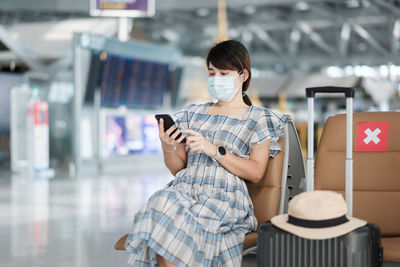 Woman wearing flu mask using smart phone sitting at airport