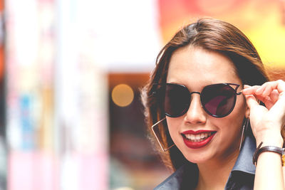 Close-up of smiling young woman wearing sunglasses in city 