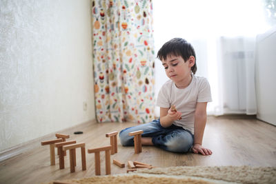 Boy caucasian brunette sad and serious plays on the floor, builds towers from wooden designer, 