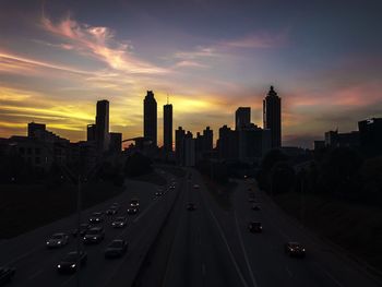 Vehicles on road amidst buildings against sky during sunset