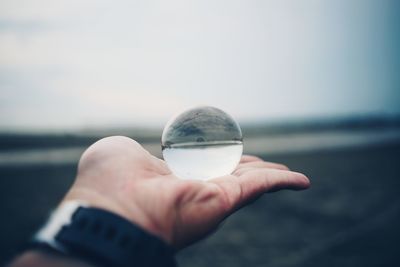 Close-up of hand holding crystal ball against sea