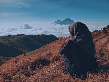 Rear view of man sitting on mountain against sky