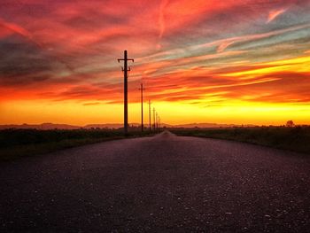 Road by electricity pylon against sky during sunset