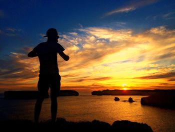 Silhouette man standing at beach against sky during sunset