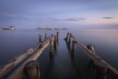 Wooden posts in sea against sky during sunset