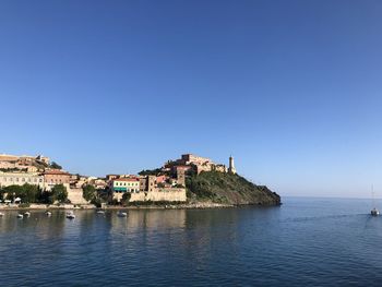 Buildings by sea against clear blue sky