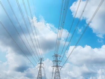 Low angle view of high voltage towers and power lines against blue cloudy sky