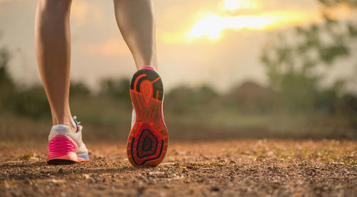 Low section of athlete wearing shoes while standing against sky during sunset