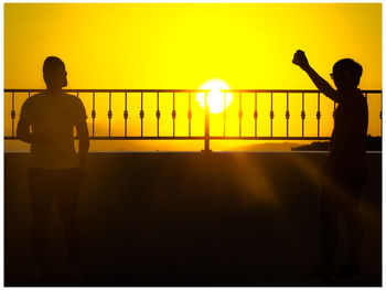 Rear view of silhouette people standing by railing against sky during sunset