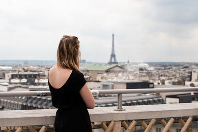 Rear view of woman looking at cityscape against sky