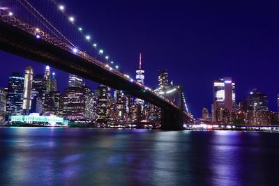 Illuminated bridge over river by buildings against sky at night