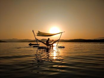 Silhouette person in sea against sky during sunset