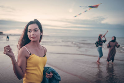 Friends enjoying at beach against sky during sunset