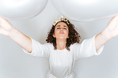 Woman blowing balloon while standing against white backgrounds