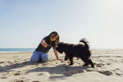 Side view of girl playing with dog  at the beach against clear sky