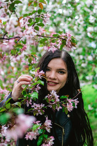 Lifestyle portrait of young smiling beautiful woman with pink apple tree flowers in rainy weather.