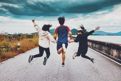 Rear view of friends jumping on water against sky