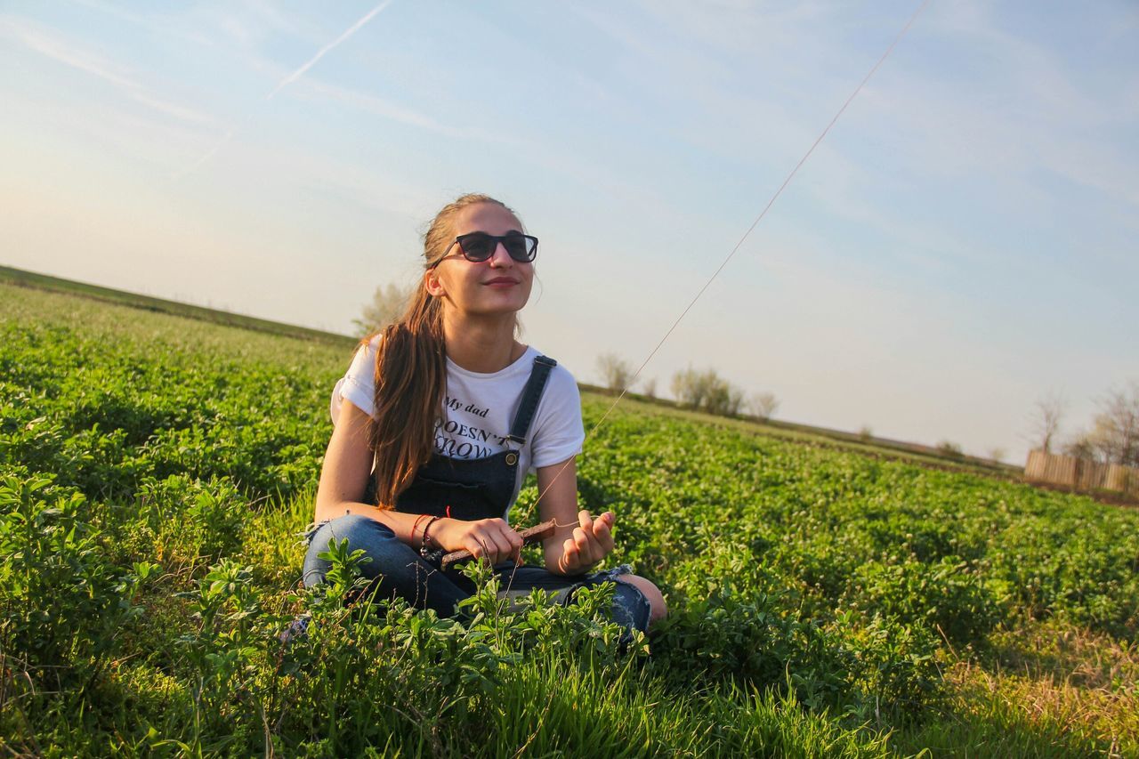 person, grass, young adult, lifestyles, casual clothing, leisure activity, portrait, looking at camera, field, smiling, sky, grassy, landscape, young women, front view, standing, full length, sunglasses