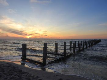 Wooden posts on beach against sky during sunset