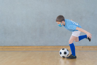 Full length of boy wearing mask playing soccer on floor