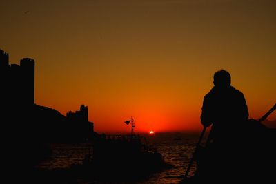 Silhouette man by sea against sky during sunset