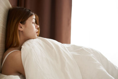 Side view of young woman sitting on bed at home