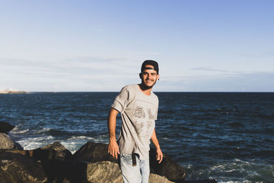 Portrait of young man standing at beach against sky