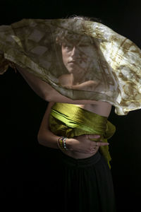 Portrait of young woman wearing mask against black background