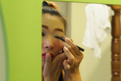 Reflection of woman applying eyeliner in mirror at home