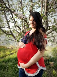 Pregnant woman with hands on stomach standing in park