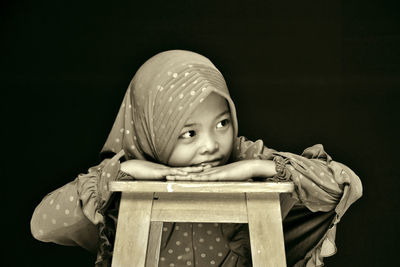 Cute girl wearing hijab looking away against black background