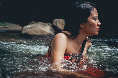 Young woman looking away while sitting on rock