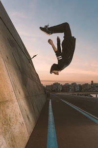 Man jumping over road against buildings and sky during sunset