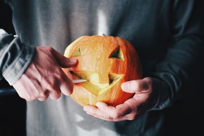 Close-up of man holding pumpkin against orange background