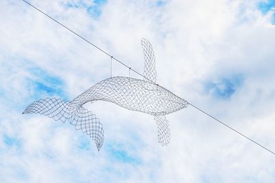 Low angle view of metallic fish decor hanging from cable against sky