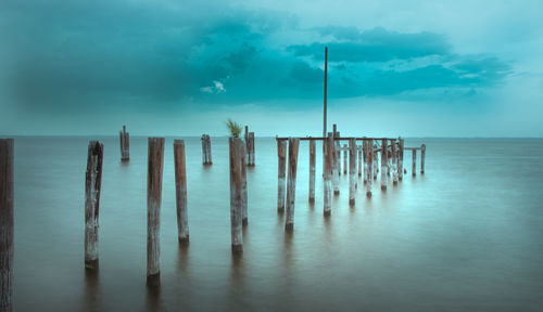 Wooden posts in sea against sky