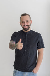 Portrait of young man gesturing thumbs up sign against white background