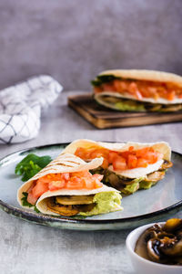 Tortilla with guacamole, fried mushrooms, tomatoes and herbs on a plate vertical view