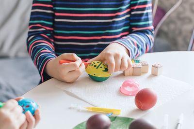 Close-up of siblings drawing on easter eggs at table