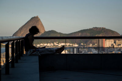 Silhouette woman sitting at balcony against clear sky